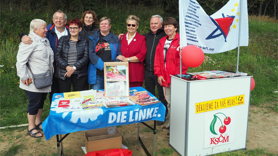 Mehrere Menschen stehen hinter einem Info-Stand mit Flyern und Zeitungen