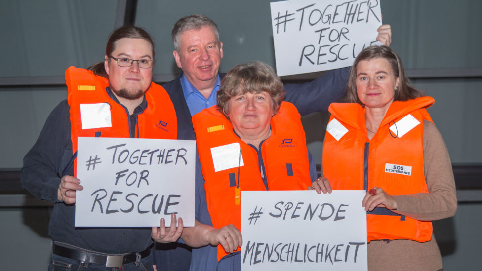 Norbert Müller, Thomas Nord, Kirsten Tackmann und Anke Domscheit-Berg tragen Rettungswesten und halten Schilder in den Händen, auf denen #SpendeMenschlichkeit und #TogetherForRescue steht