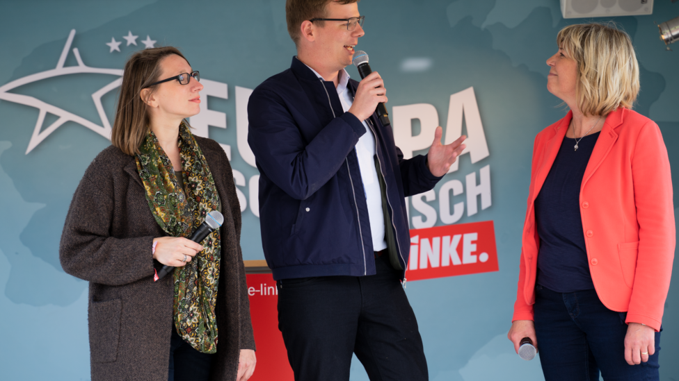 Anja Kreisel, Sebastian Walter und Kathrin Dannenberg stehen mit je einem Mikrofon in den Händen vor einer Wand mit dem Logo der LINKEN