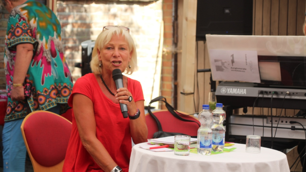 Dagmar Enkelmann sitzt mit einem Mikrofon in der Hand an einem runden Tisch, auf dem Wasserflaschen stehen