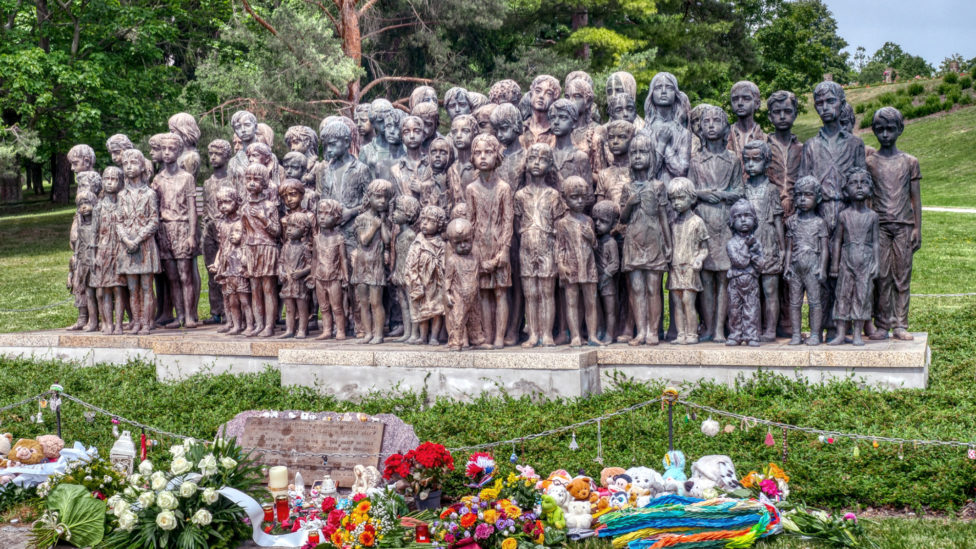 Eine Gruppe Bronzestatuen von Kindern, vor denen Blumen und Grablichter stehen
