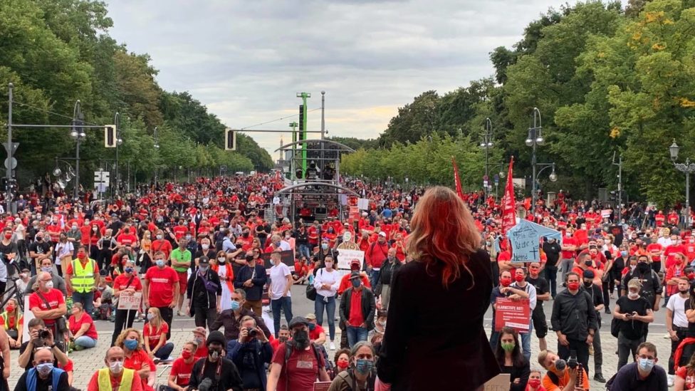 Caren Lay steht auf einer Bühne vor einer Menschenmenge, von denen viele ein rotes T-Short oder eine rote Weste tragen