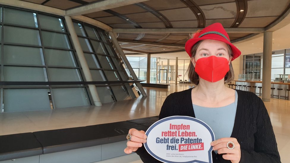 Anke Domscheit-Berg stehtmit einer Mund-Nase-Bedeckung in den Räumlichkeiten des Bundestags und hält ein Schild in Form einer Sprechblase, auf dem dem "Impfen rettet Leben. Gebt die Patente frei. DIE LINKE." zu lesen ist
