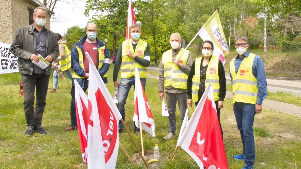 Mehrere Menschen mit Warnwesten und Mund-Nase-Bedeckung, die Fahnen mit Verdi-Logo tragen