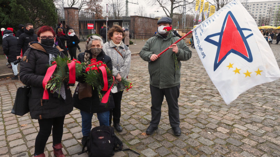 Gruppenbild der LAG Netzwerk EL vor dem Friedhof der Sozialisten in Berlin-Friedrichsfelde, eine Person hält eine Fahne mit dem Logo der Europäischen Linken