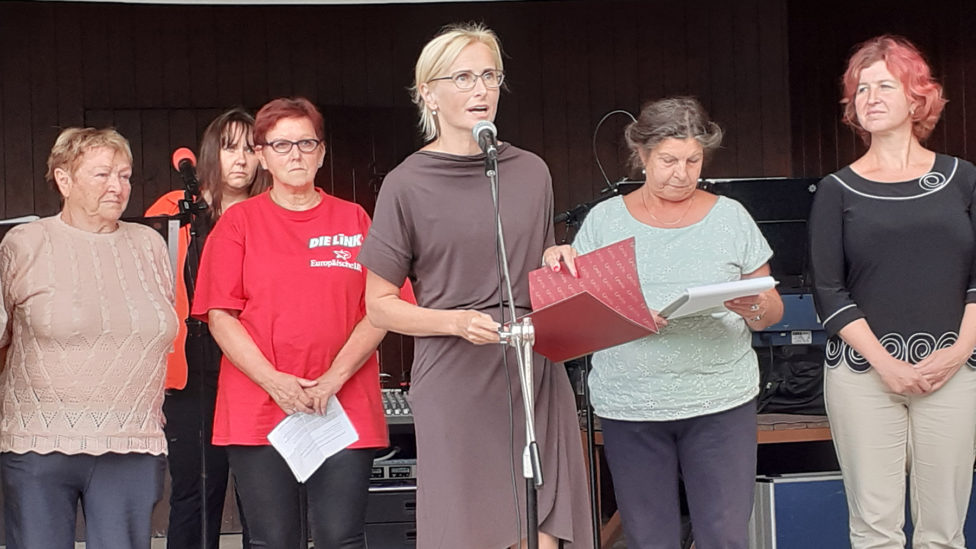 Mehrere Personen stehen auf einer Bühne, darunter Kateřina Konečná am Mikrofon und Monika Schömmel