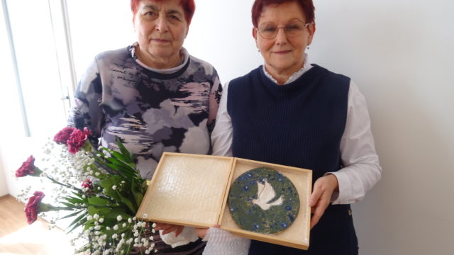 Alena Grospičová und Monika Schömmel stehen nebeinander und halten gemeinsam einen Keramikteller mit einer Friedenstaube in die Kamera